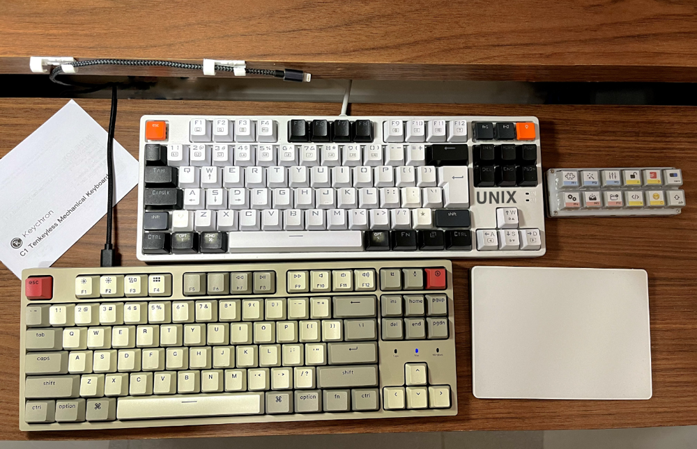 Foto da bancada com 2 teclados mecânicos conectados a cabos USB, um trackpad e um teclado de macros.