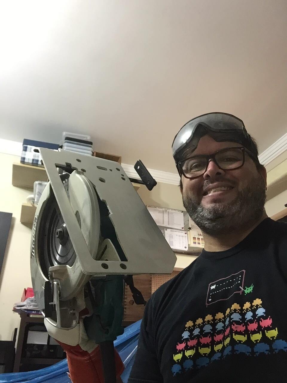 Foto minha segurando uma serra circular, com oculos de proteção e camiseta da academia dos space invaders