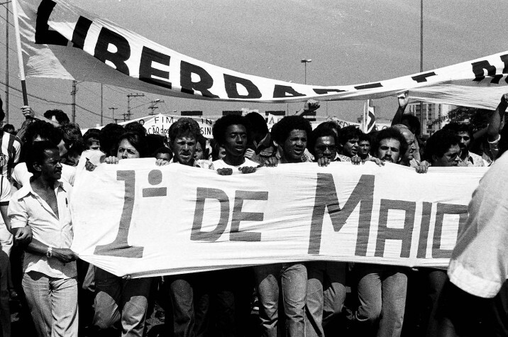 Foto em preto e branco de um movimento grevista brasileiro com uma faixa onde se lê a palavra Liberdade, e outra onde está escrito 1º de Maio