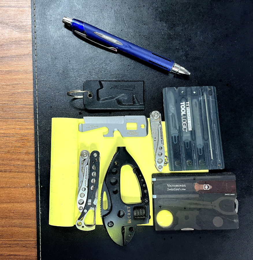 5 multiferramentas de pequeno porte, sobre um bloco de post-it de grande porte, com uma caneta para servir de escala