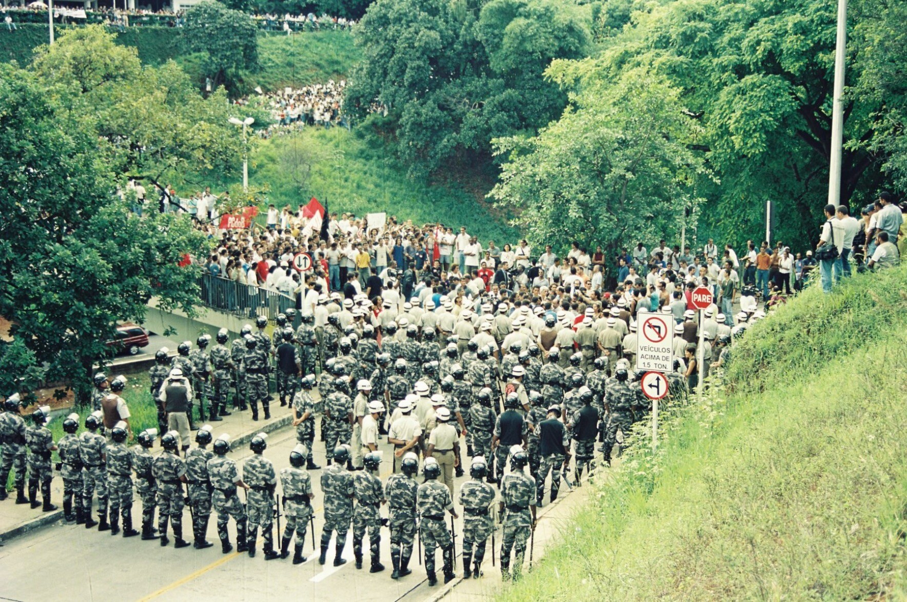 Foto mostrando a manifestação chegando e a PM, formada, aguardando.