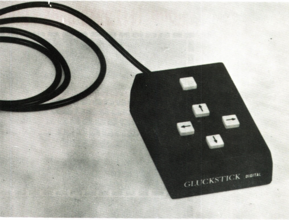 Foto em preto e branco, publicada por uma revista da época, do Gluckstick Digital, uma caixinha com 4 botões direcionais e um quinto botão, sem, rótulo.