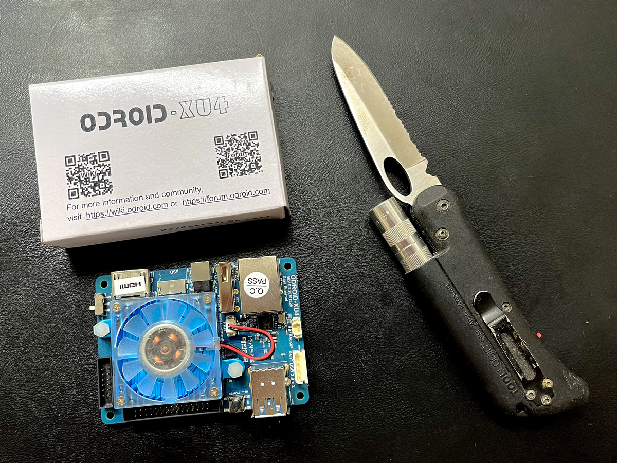 Uma placa Odroid XU4, ao lado da sua caixa e do canivete usado para abrir o pacote que o trouxe.