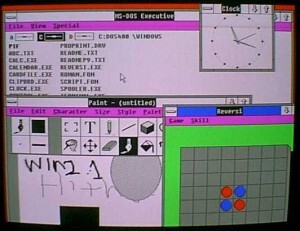 Foto de um monitor com o WIndows 2.10, exibindo o Paint, o jogo Reversi, e o prompt do MS-DOS