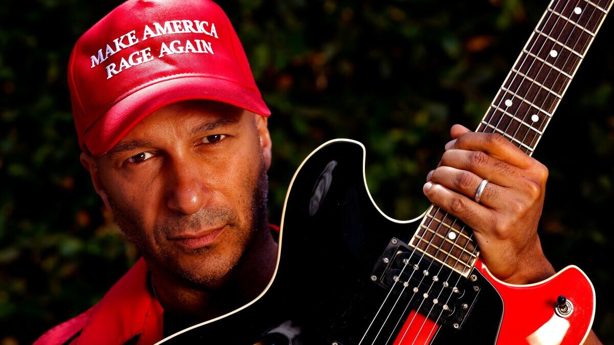 Tom Morello segurando uma guitarra e com um bonê que diz “make america rage again“