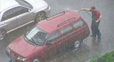 Foto de homem, com mangueira em punho, lavando um carro, na chuva