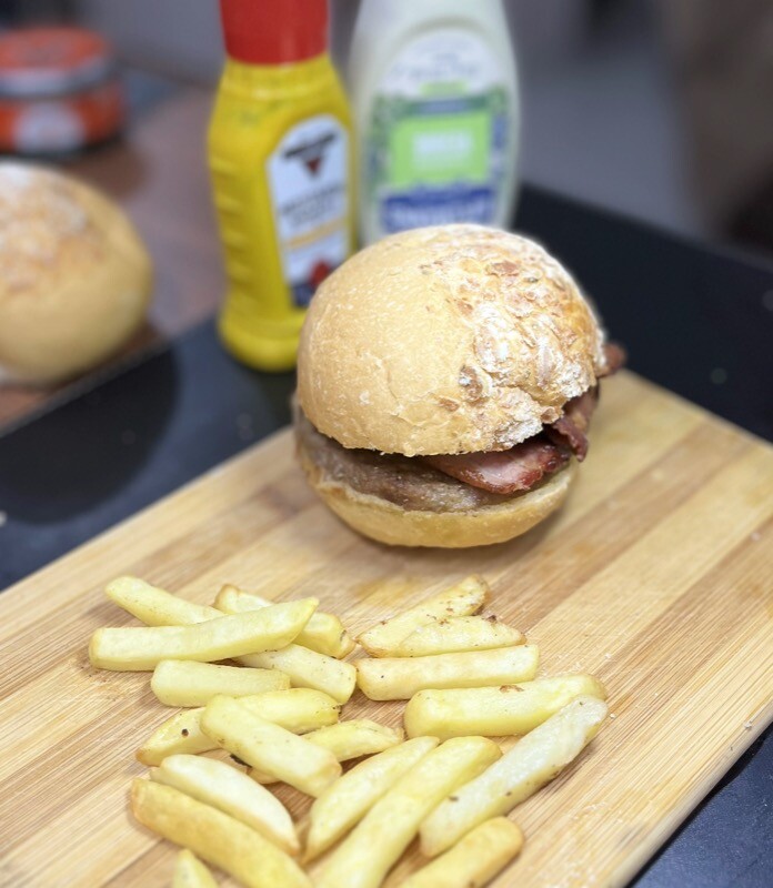 Um hambúrguer com bacon, e batatinhas ao redor