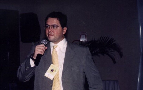 Foto minha, de paletó e gravata, microfone em punho, em Manaus/2003