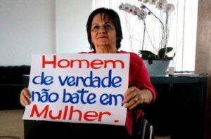 Maria da Penha segurando um cartaz escrito Homem de Verdade Não Bate em Mulher