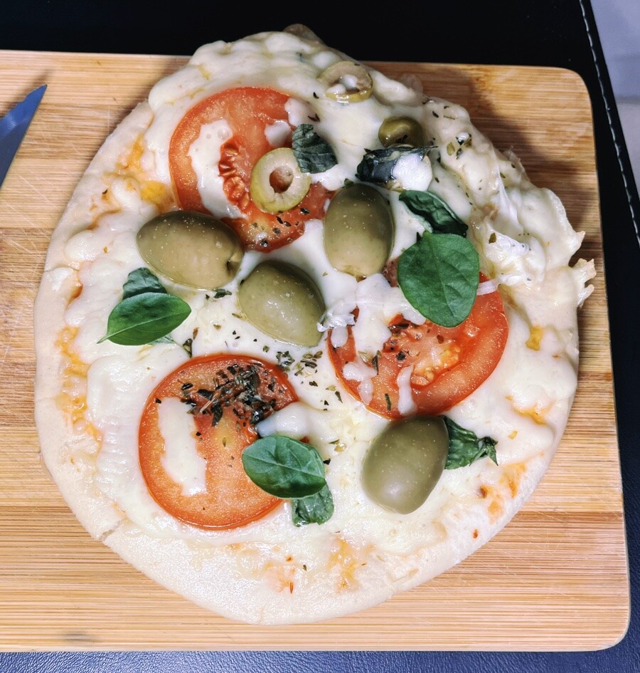 mini-pizza margherita com adicional de azeitonas, tomates fatiados, manjericão, servida sobre uma tábua