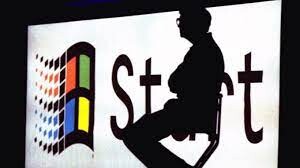 Silhueta de Bill Gates no palco em frente a um painel mostrando o menu Start, do Windows 95