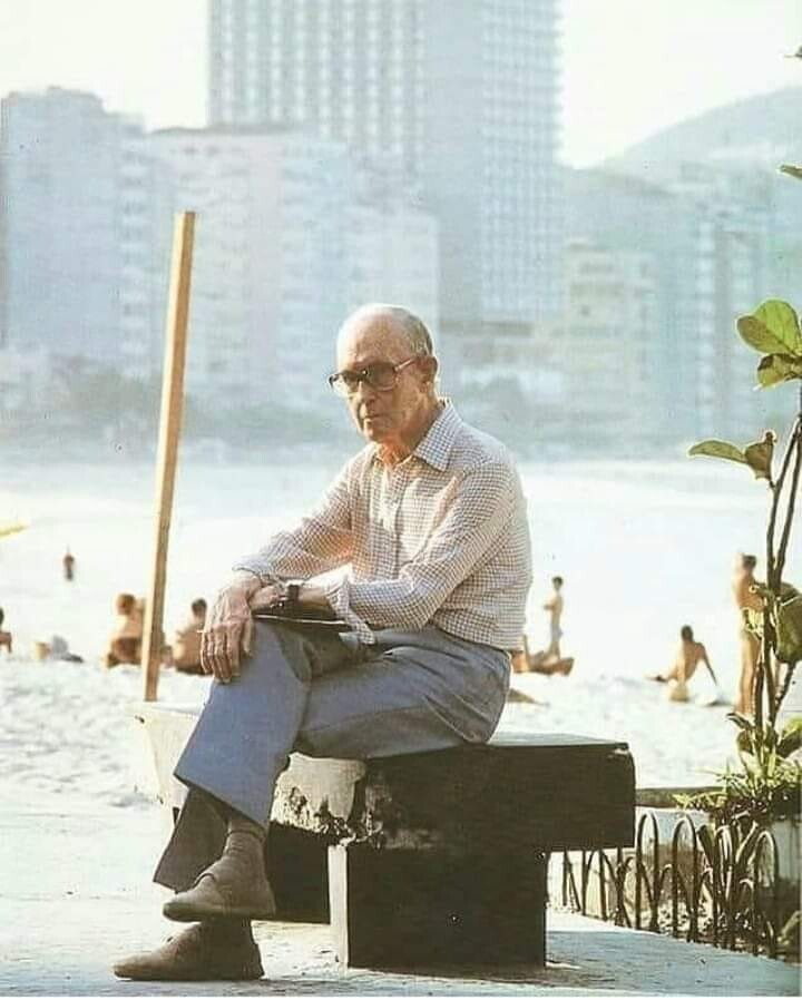 Drummond em pose que acabaria eternizada em monumento, sentado em banco na orla carioca