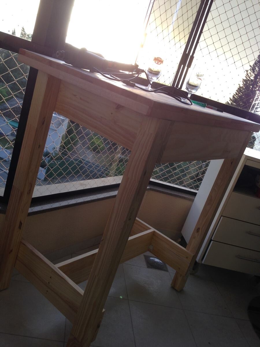 Uma mesa alta de madeira, recem-concluida, ainda não pintada, com ferramentas e 2 copos de cerveja sobre ela, numa sacada, ao por do sol