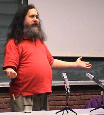 Richard Stallman abre os braços em frente a 2 microfones