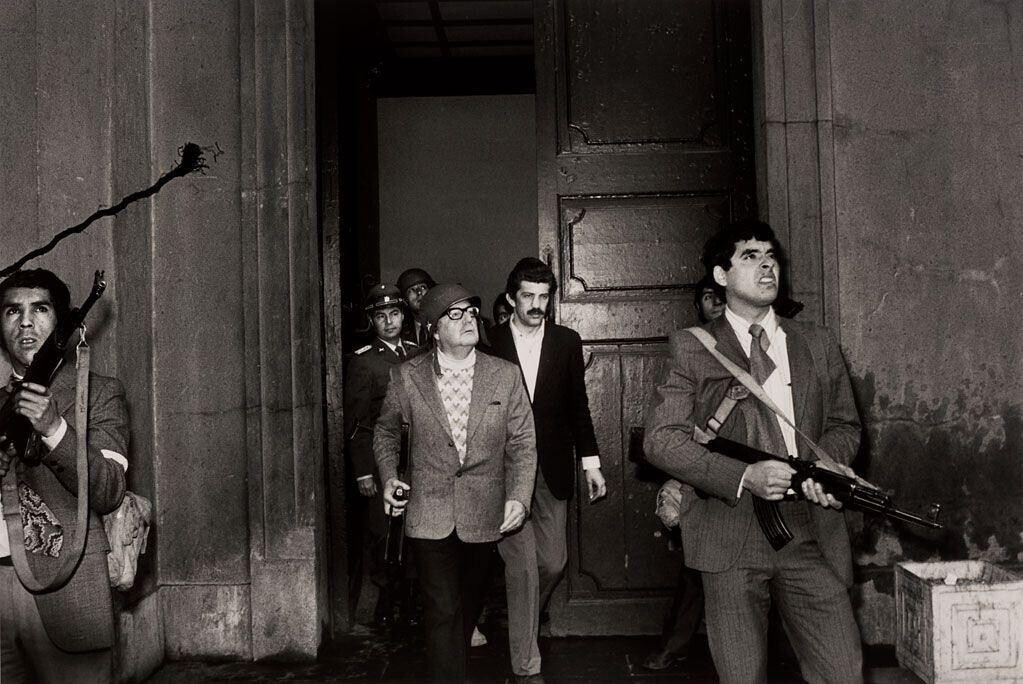 Na última fotografia com vida, Allende observa os ataques aéreos contra a sede do governo, segurando um fuzil e usando um capacete, cercado por seu aparato de segurança.