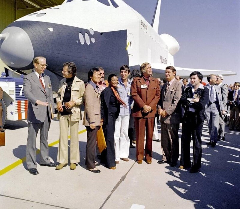 O Enterprise ao fundo e, perfilados, o gestor da NASA, James C. Fletcher, e vários integrantes do elenco da série original de Jornada nas Estrelas, e seu criador.<br>