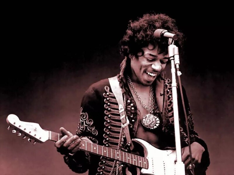 Jimi Hendrix sorri no palco, com a guitarra em punho