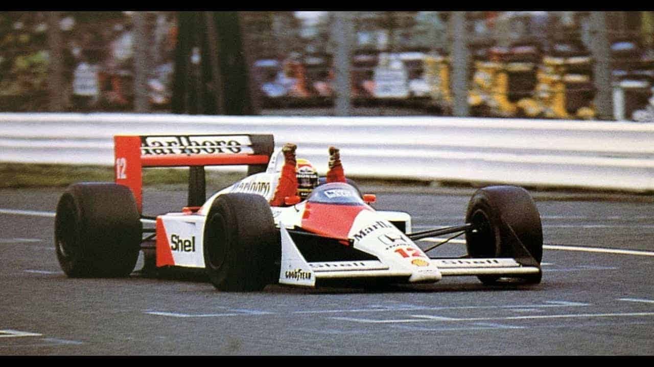 Senna ergue os 2 braços, ainda dentro do carro, comemorando o resultado