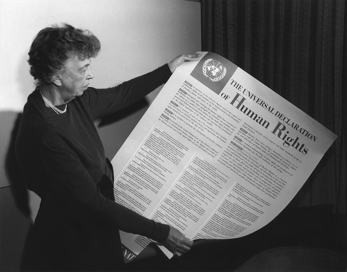 Eleanor Roosevelt segura e observa uma versão da Declaração em formato cartaz.<br>