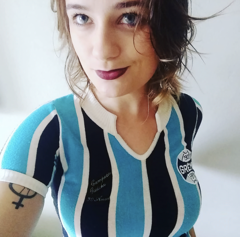 A aniversariante Mari, maquiada e de camisa comemorativa de 30 anos de uma conquista do Grêmio, sorri para a câmera e olha para o alto