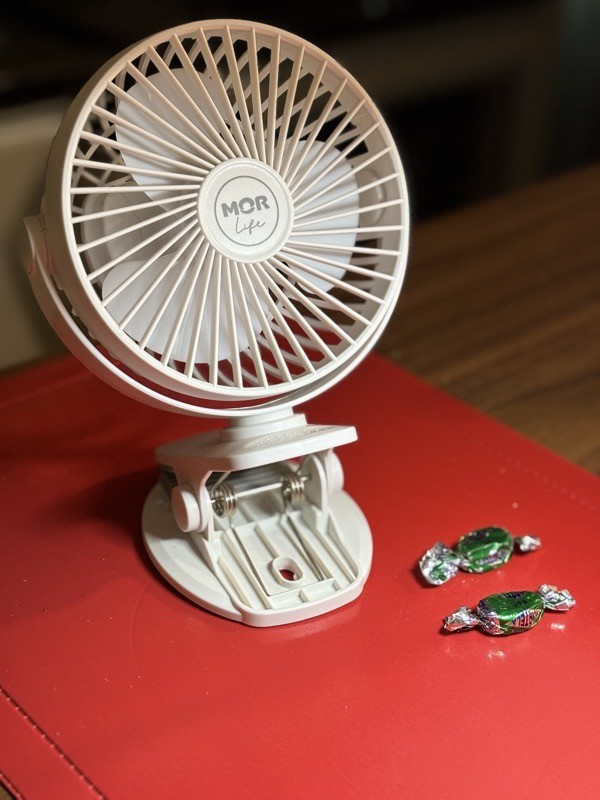 Um ventilador plástico, de 3 pás, com cerca de 20 centímetros de altura, em cor branca, com a marca Mor Life, sobre um fundo vermelho e ao lado de duas balas de hortelã