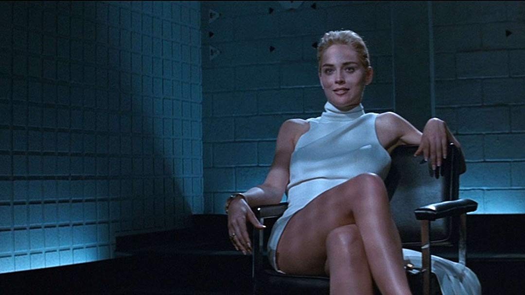 Após topar prestar depoimento ao investigador Nick Curran (Michael Douglas) sobre a morte do roqueiro aposentado Johnny Boz – esfaqueado com um furador de gelo –, a escritora Katherine Tramell (Sharon Stone) está confortavelmente sentada em uma cadeira, de pernas cruzadas, trajando um vestido branco e curto, na sala de interrogatório.<br>