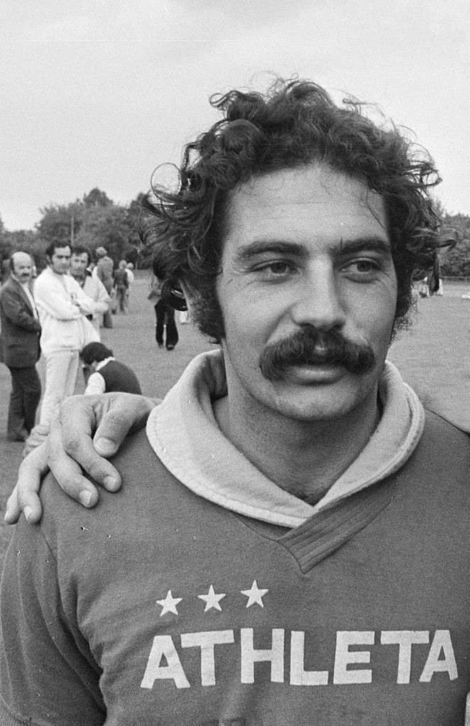 Roberto Rivellino com traje atlético, em campo durante treinos, com uma mão posicionada sobre seu ombro.