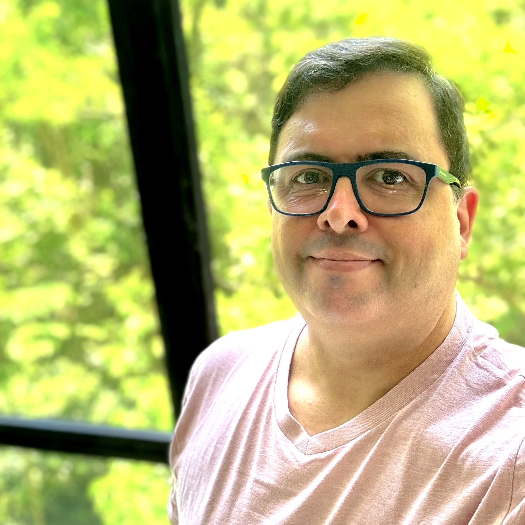Selfie minha olhando para a câmera, de camiseta rosa, com vegetação ao fundo