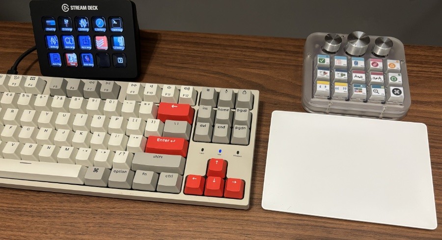 Um tampo de fórmica com um teclado Keychron C1, um Stream Deck de 15 botões, um teclado de atalhos com 15 teclas e 3 dials giratórios, e um trackpad sem fio