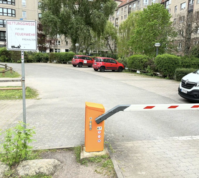 Foto da cancela de acesso a um estacionamento pavimentado e semi-vazio 