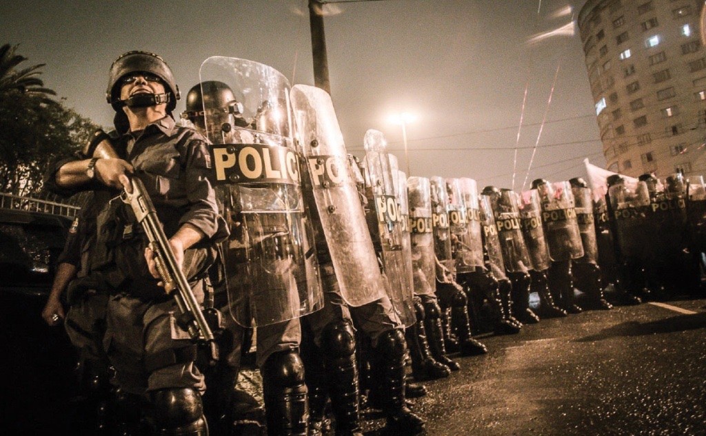 Polícia militar em formação tática de choque, com escudos transparentes.