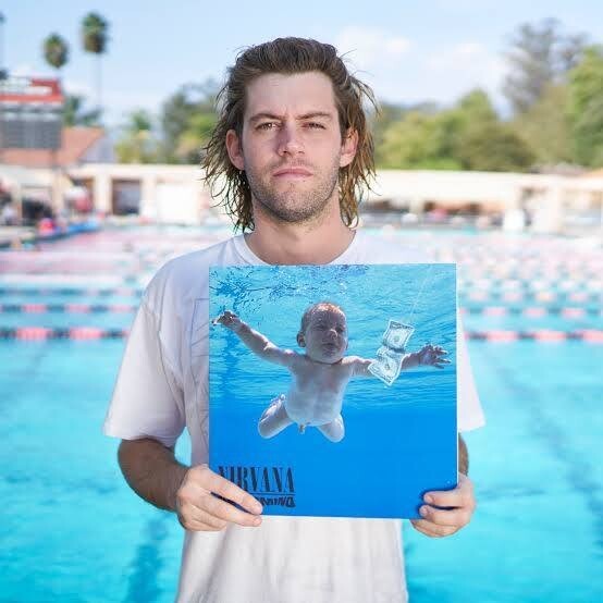 O modelo, já adulto, segura a capa do disco, na beira de uma piscina