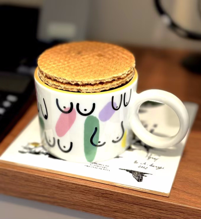Uma xícara com decoração de peitos, na qual foram empilhados 2 biscoitos tipo stroopwafel