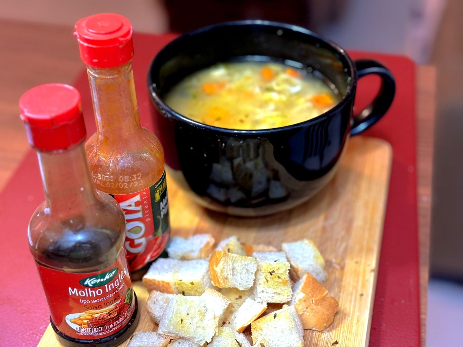 Uma canja de galinha servida ao lado de cubinhos de pão e de garrafinhas de molho inglês e de molho de pimenta