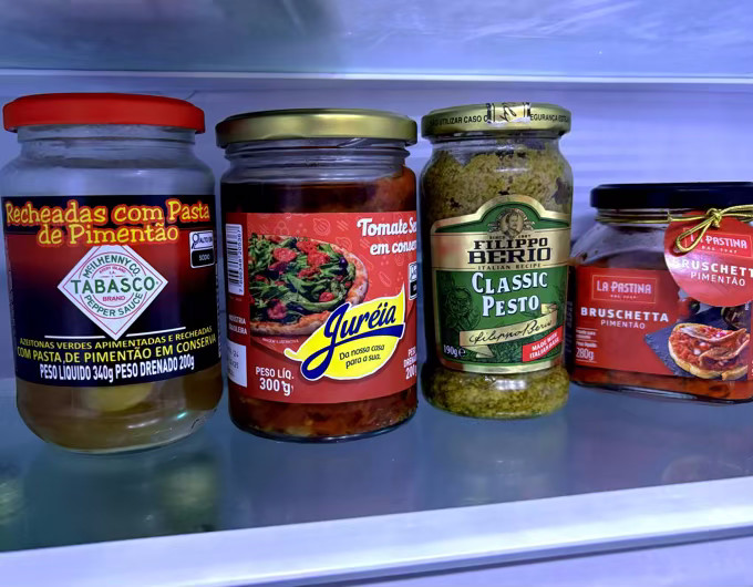 4 vidros de conserva lado a lado em uma prateleira de geladeira. Em um deles o rótulo diz: Azeitonas recheadas com pasta de pimentão Tabasco