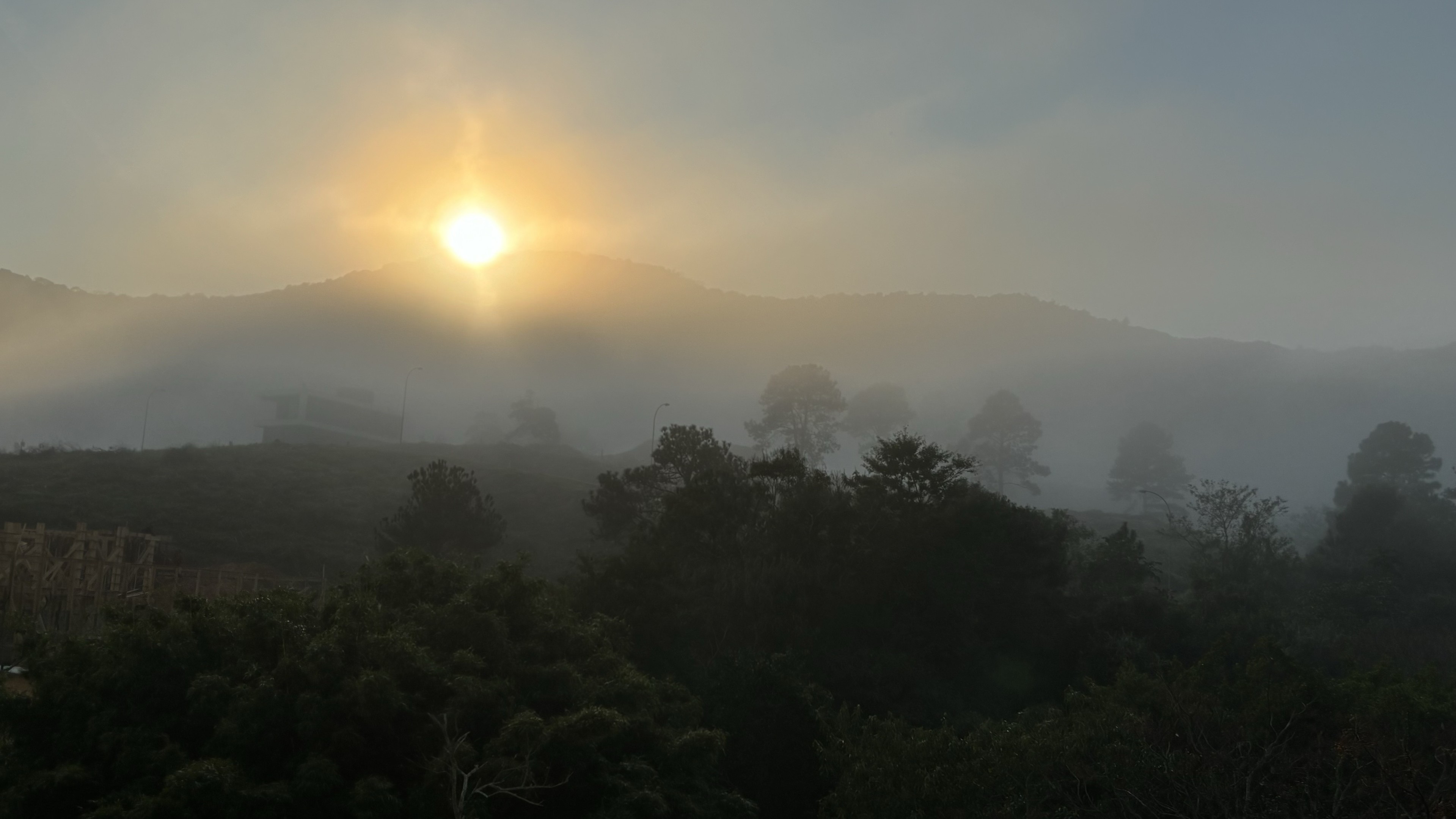 Sol nascendo por trás dos morros e matas cobertas por névoa