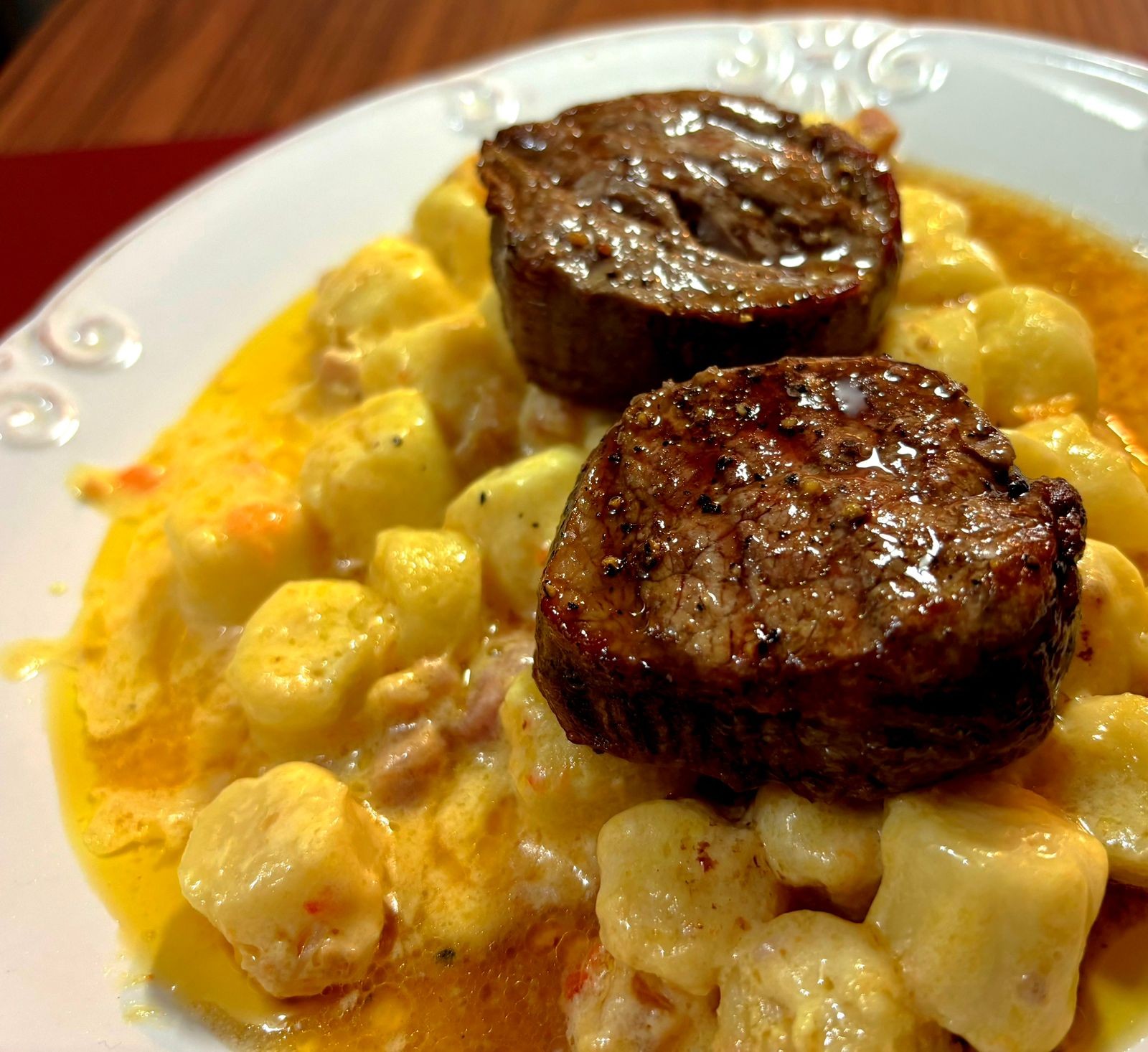 Um prato servido com 2 medalhões de carne bovina sobre uma porção de nhoque com molho de nata