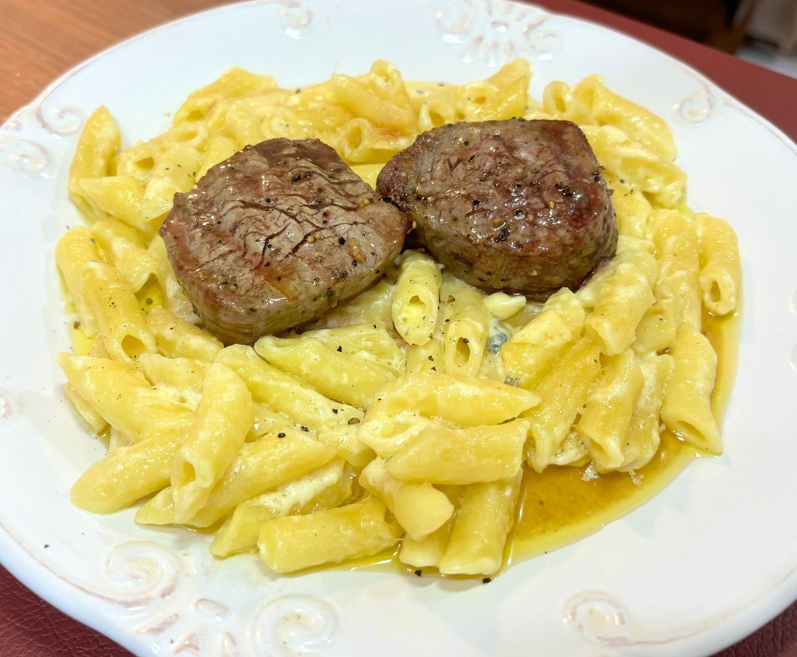 dois medalhões de carne bovina preparados na manteiga e com bastante pimenta do reino moída, servidos sobre um prato de penne ao molho de 4 queijos