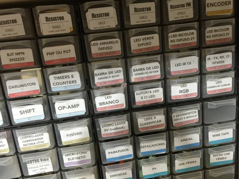 Cerca de 40 gavetinhas de miudezas, com etiquetas coloridas identificando itens como transistor 2N2222, resistor de 560 ohms, led amarelo difuso, sindl, microfone eletreto e muito mais
