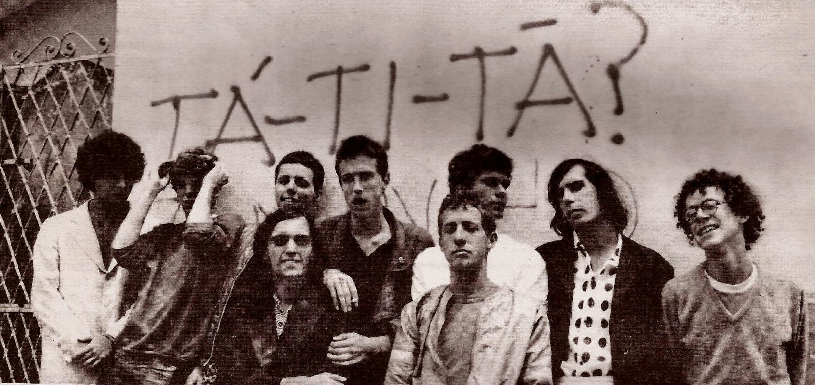 Foto em preto e branco dos jovens integrantes dos Titãs, sob uma pichação dizendo: “TÁ-TI-TÃ?“