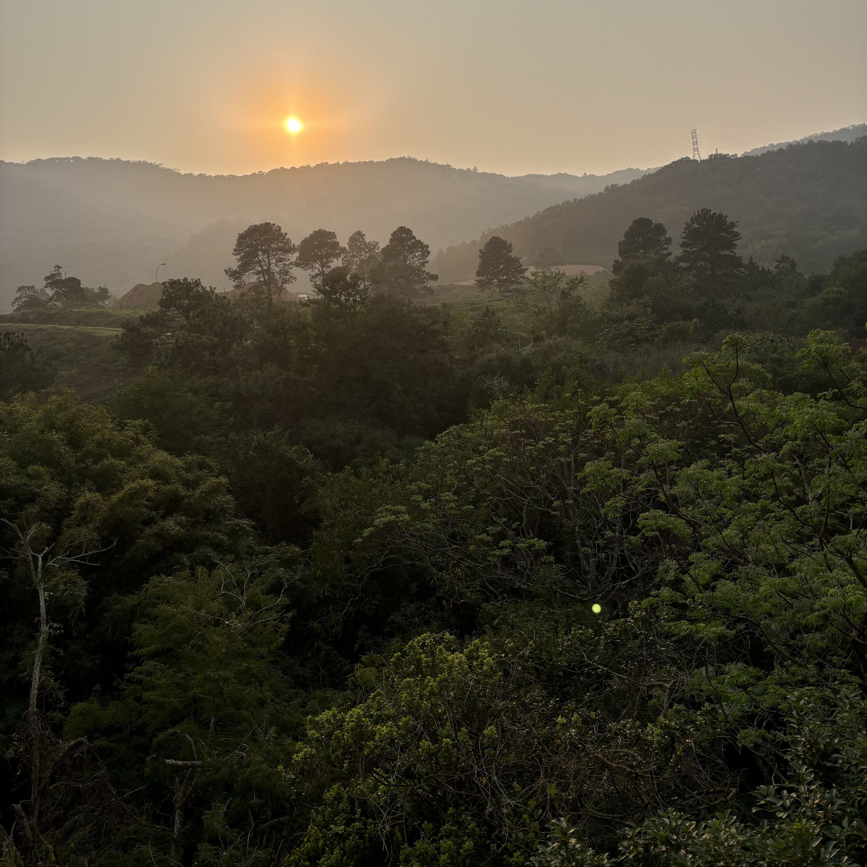 Sol nascendo por trás de morros cobertos de fumaça 