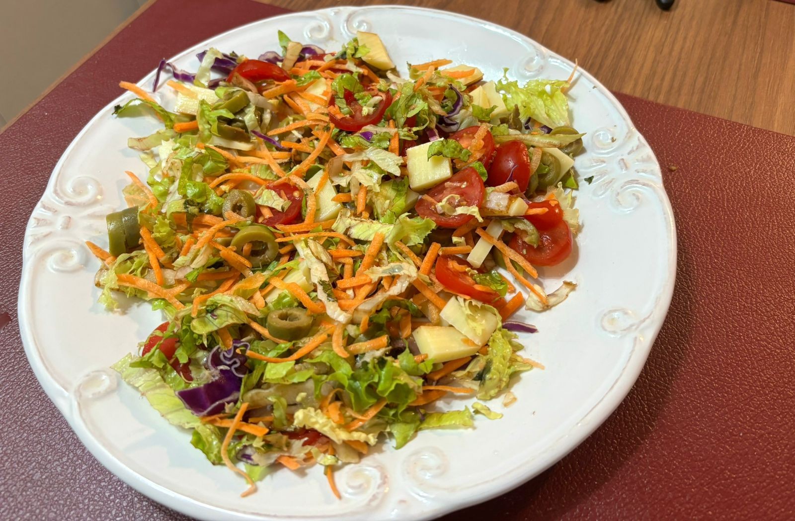 Um prato de salada de folhas picadas, cenoura ralada, azeitonas e queijos