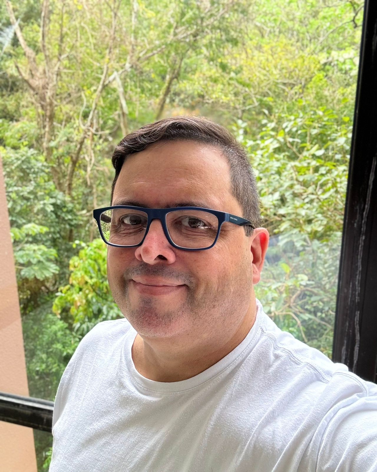 Selfie minha olhando para a câmera, mostrando o corte de cabelo com a lateral aparada, e tendo ao fundo a mata