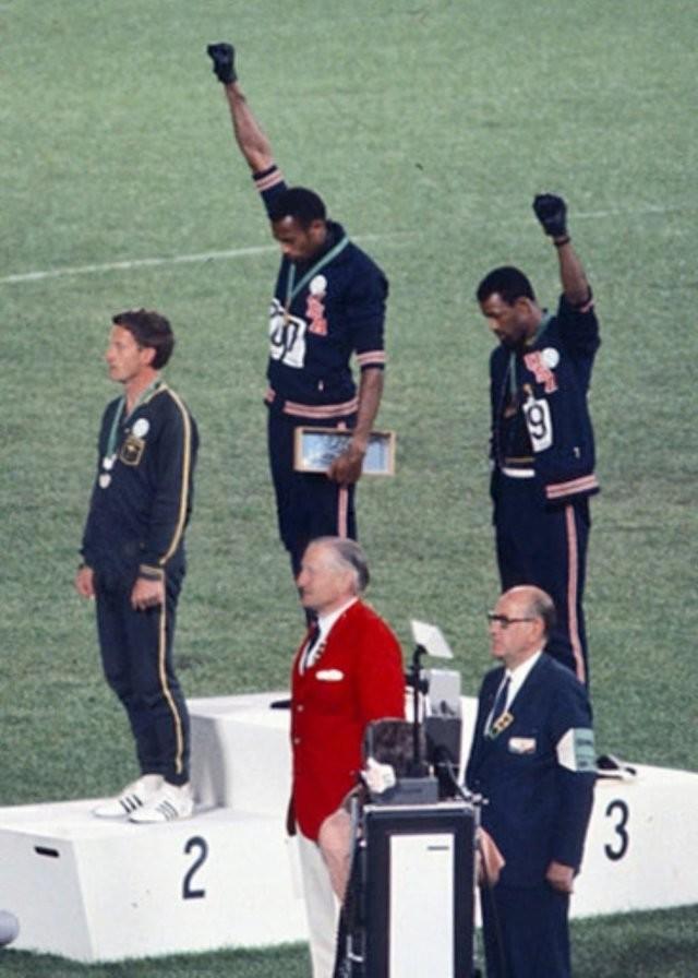 O medalhista de ouro Tommie Smith (centro) e o medalhista de bronze John Carlos (direita) mostrando o punho erguido, em saudação, no pódio após a corrida de 200m nos Jogos Olímpicos de Verão de 1968
