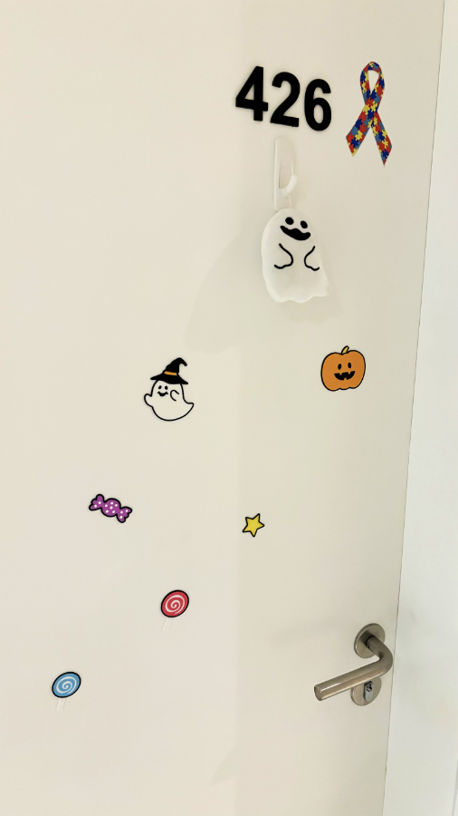 Uma porta de apartamento, com o símbolo do autismo, um fantasminha pendurado, e adesivos de fantasma, abóbora e doces