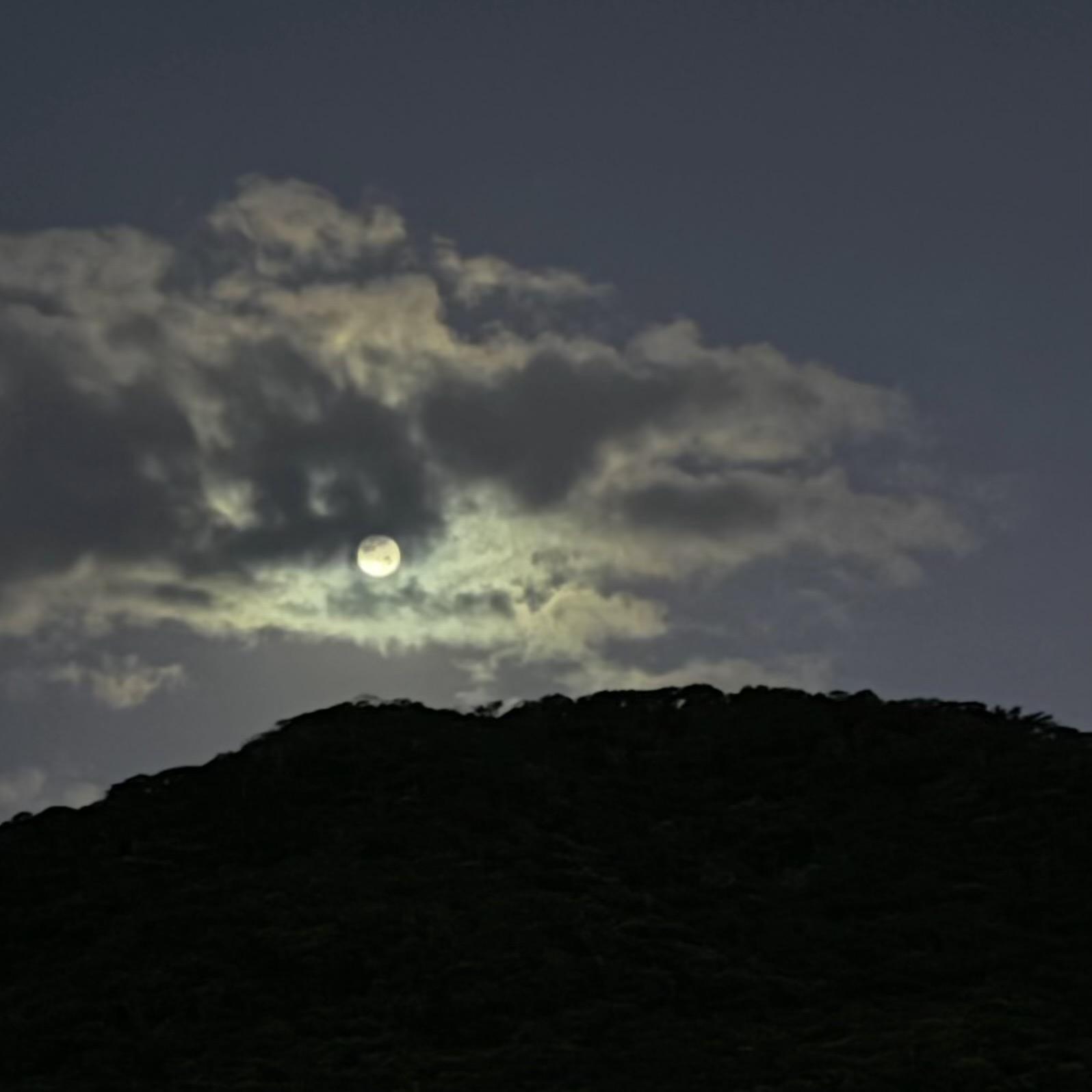 A lua bem redonda e iluminada, entre nuvens, acima dos morros