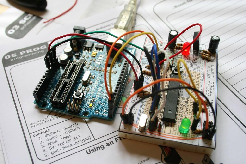 Lado a lado (e conectadas entre si), uma placa Arduino oficial (em modelo antecessor ao clássico Arduino Uno) e um Arduino genérico montado a partir de um esquema impresso em papel e sobreposto a uma breadboard.