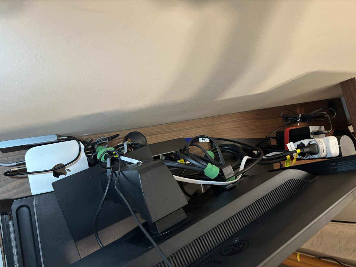 Foto tirada de cima dos 2 monitores, mostrando sua parte traseira, com várias espiras de cabos HDMI e de força, fixados com tiras de velcro e presas a suportes atrás dos monitores, onde também está uma régua de 3 tomadas.<br>