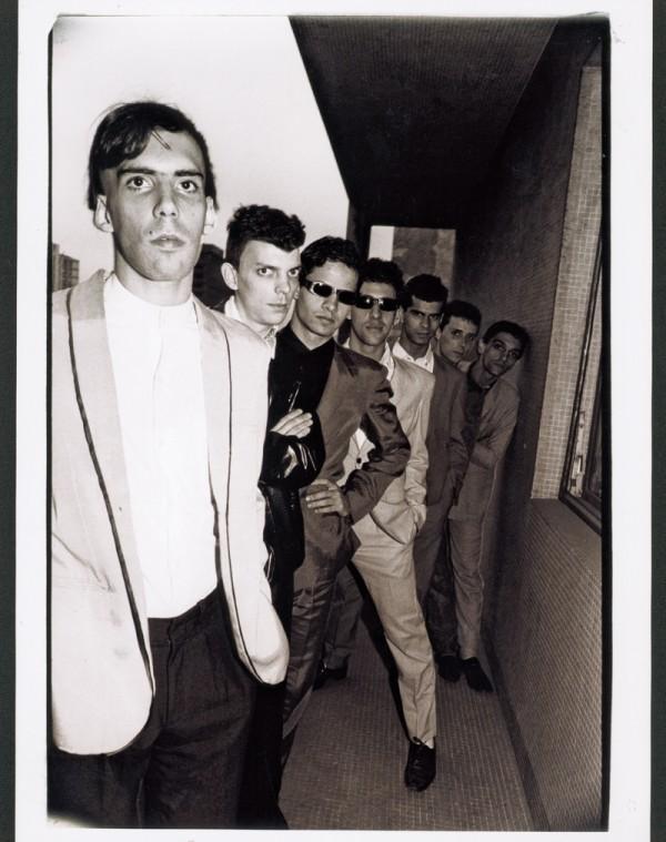 Foto em preto e branco do Jovem Arnaldo Antunes à frente dos demais Titãs, enfileirados