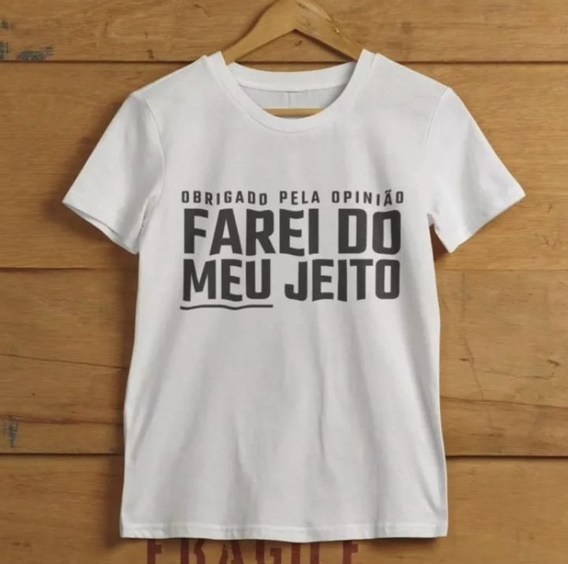 foto comercial de uma camiseta branca pendurada em um cabide. A estampa diz:<br><br>obrigado pela opinião<br>FAREI DO MEU JEITO